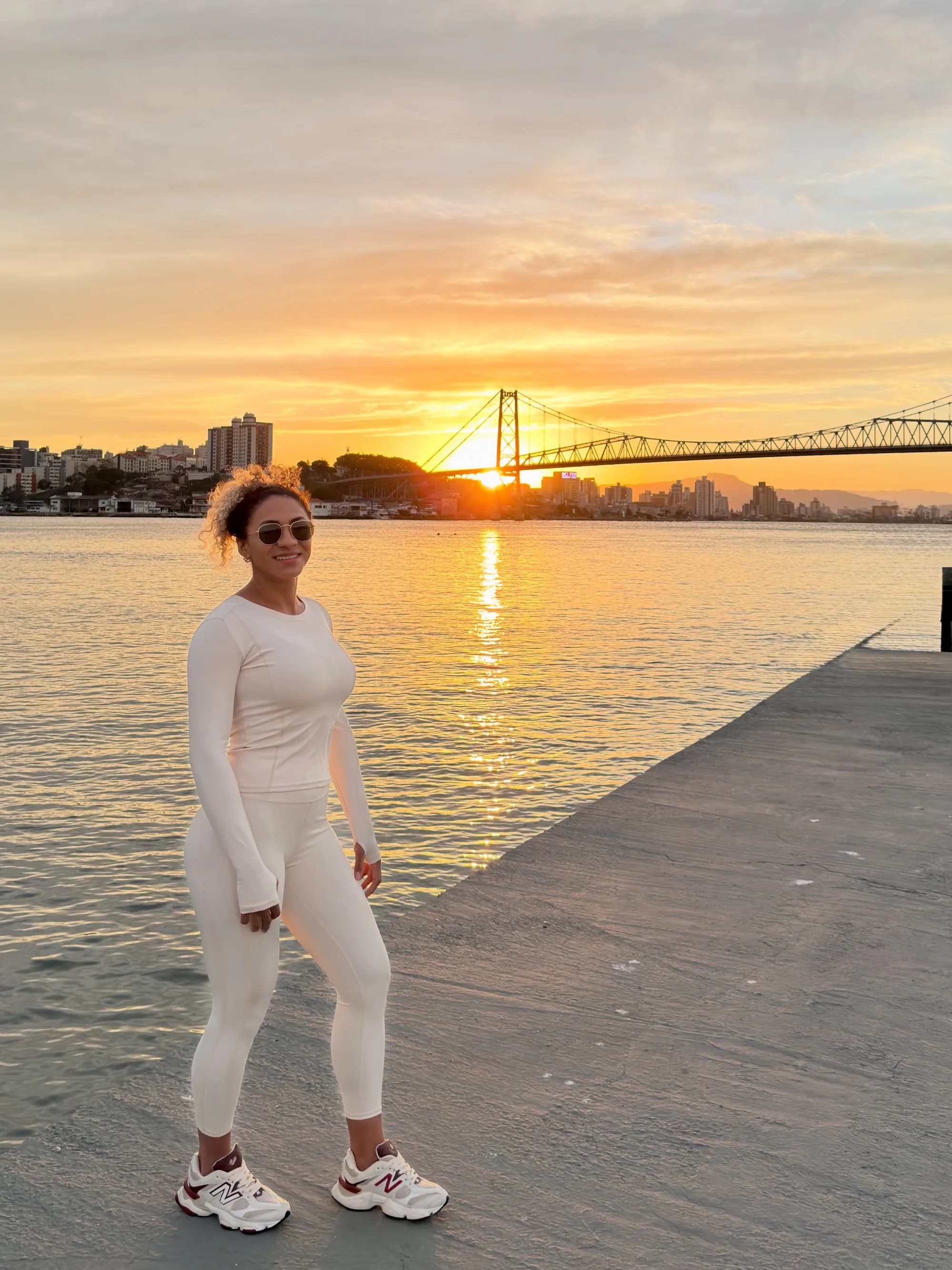 Conjunto off-white no pôr do sol da beira-mar, com a Ponte Hercílio Luz ao fundo